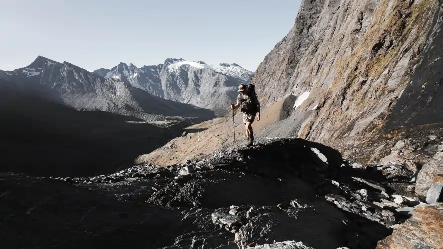 Man with hiking pole and ultralight gear standing in New Zealand mountains, Thru-Hiking text overlay