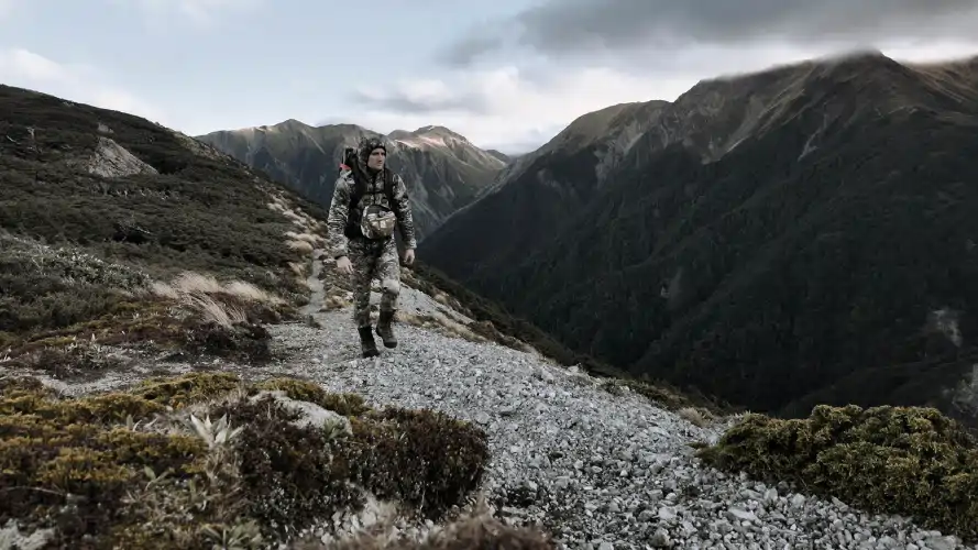 Man in hunting gear with backpack walking a mountain trail in New Zealand, Hunting Gear text overlay